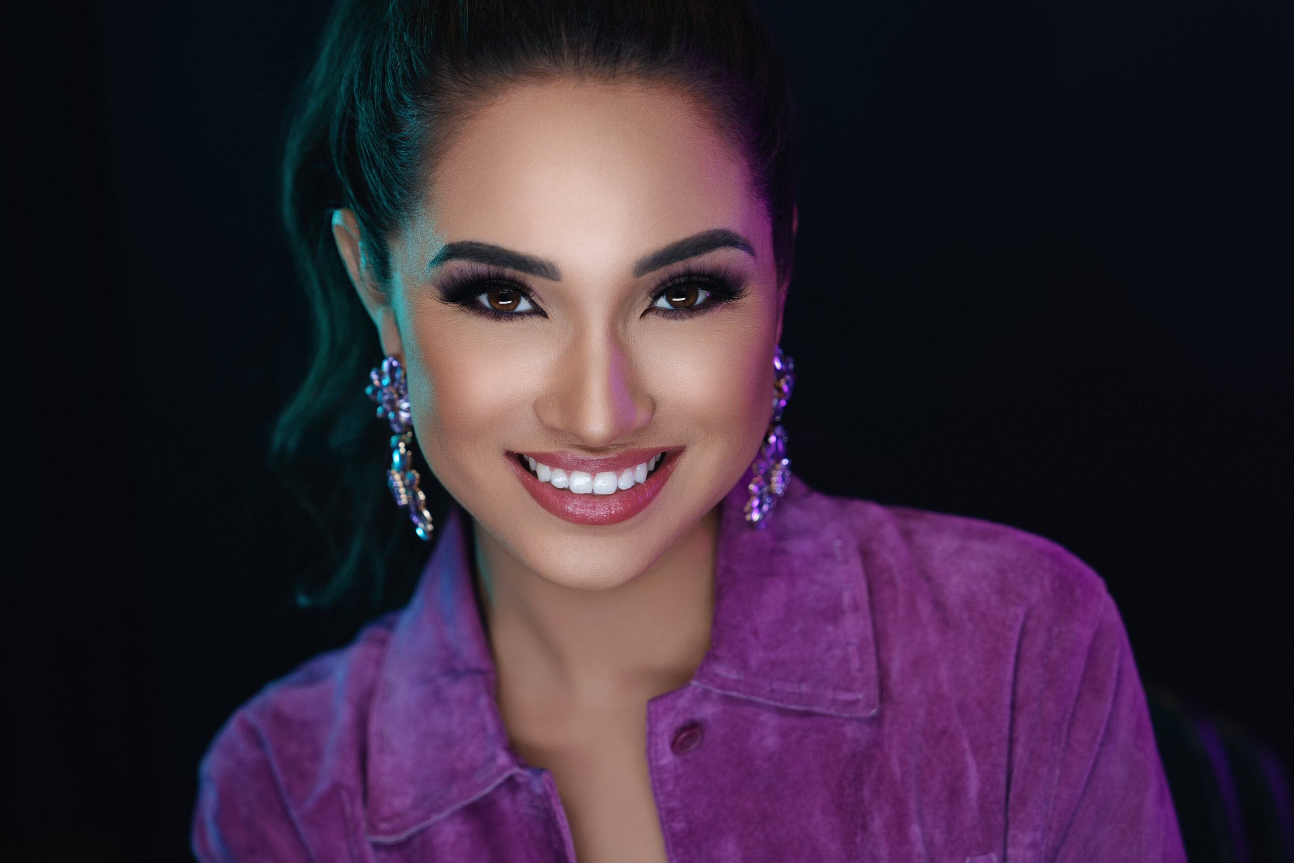 Polished professional woman wearing a bold purple suede jacket and crystal statement earrings, perfect outfit inspiration for a modern headshot session