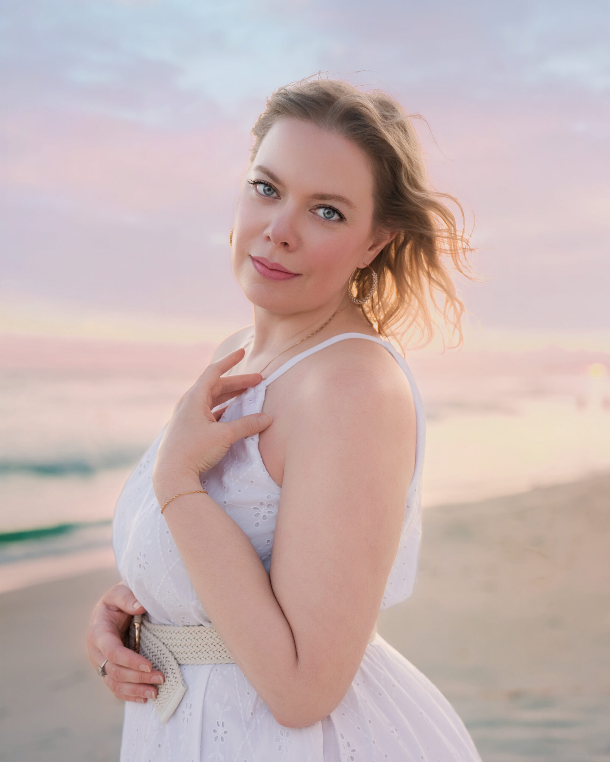 Elegant beach portrait of Breanne Cook, Birmingham, Alabama fine art photographer behind Breanne Fine Portraiture, wearing a white sundress at sunset with the ocean in the background.