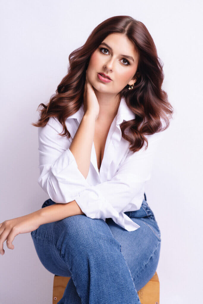 Professional LinkedIn headshot in Birmingham, AL featuring a confident young woman in a white blouse and jeans, seated against a clean white background.