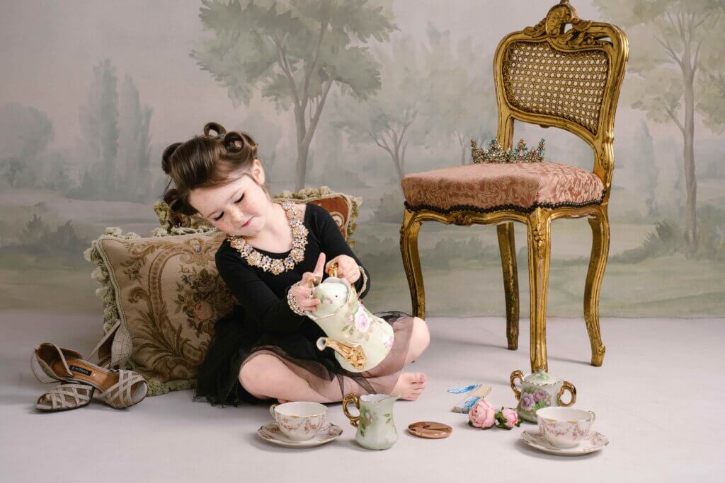 Five-year-old girl in pin curls and a black tutu pouring tea from a vintage china teapot during a playful princess tea party portrait in Birmingham, Alabama