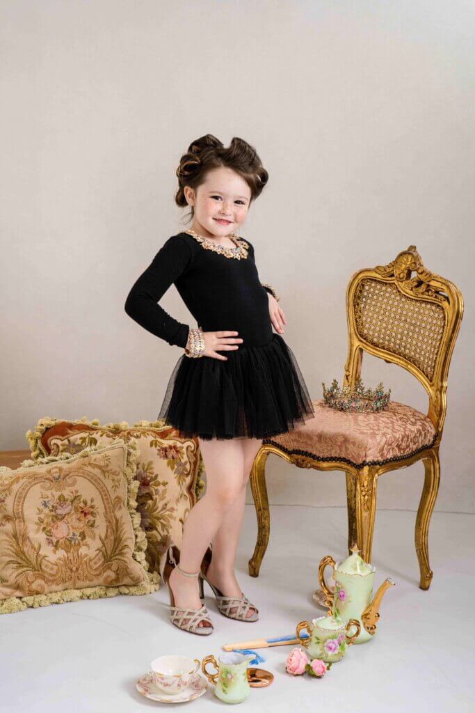 Little girl trying on sparkly dress-up heels at a vintage tea party set during a children's portrait session in Trussville, Alabama
