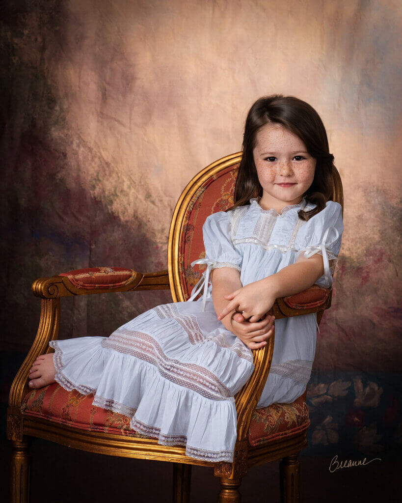 Five-year-old girl in a pale blue heirloom lace dress standing beside a gilded French chair for a classic children's portrait in Birmingham, Alabama