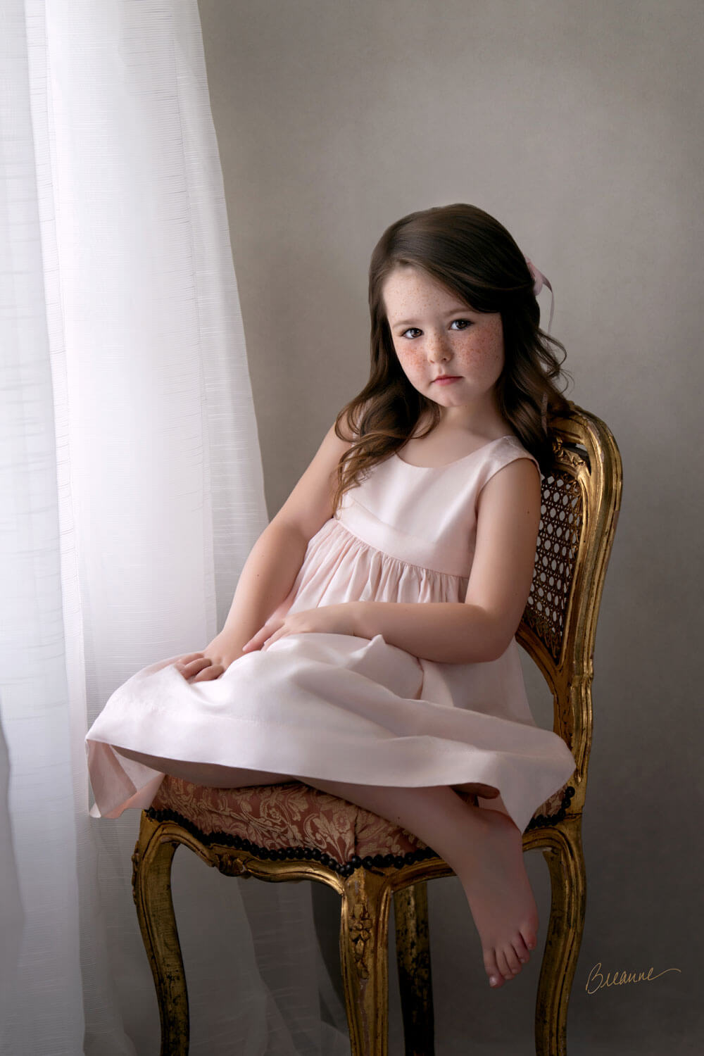 Five-year-old girl with freckles seated on a gilded French chair in soft window light during a children's heirloom portrait session in Birmingham, Alabama