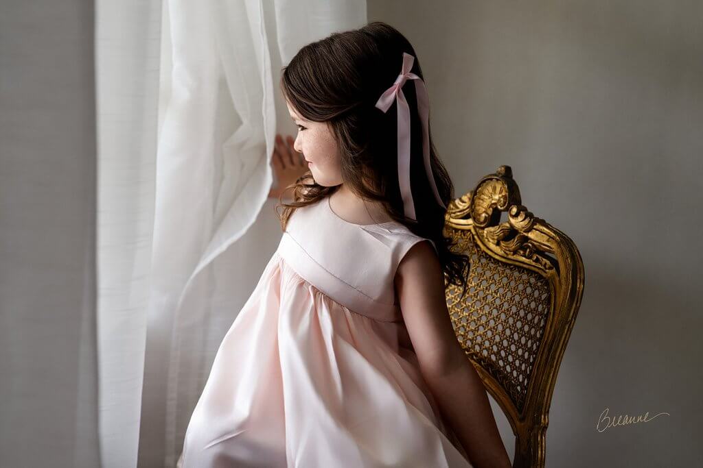 Four-year-old Callaway in a pale pink dress beside a softly lit studio window and gilded French chair in Trussville, Alabama.