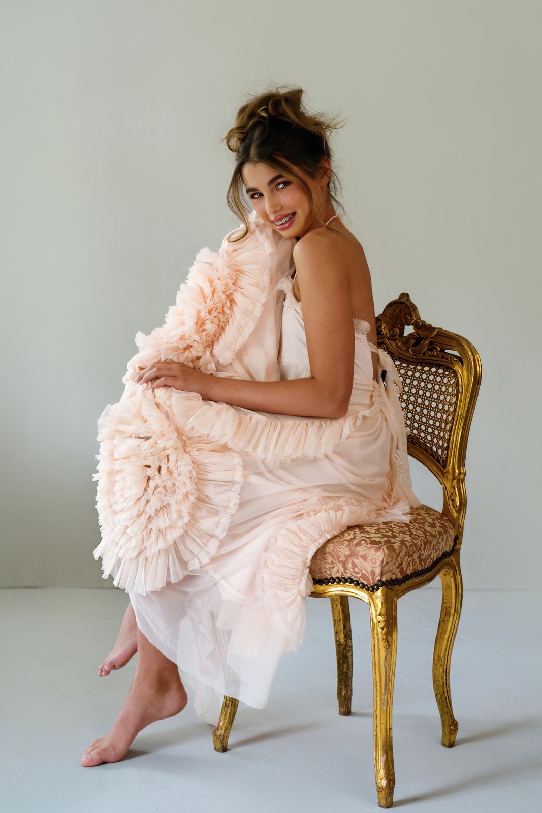Ireland sits on a antique french gold gilded chair in a soft, peach whimsical dress during her modeling portfolio session with Breanne Fine Portraiture in Birmingham Alabama