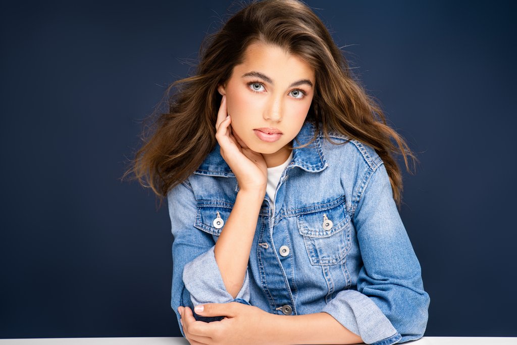 A young girl with brown hair wearing a denim jacket and white T-shirt against an aquamarine-blue backdrop in Breanne Cook's portrait studio in Birmingham Alabama.